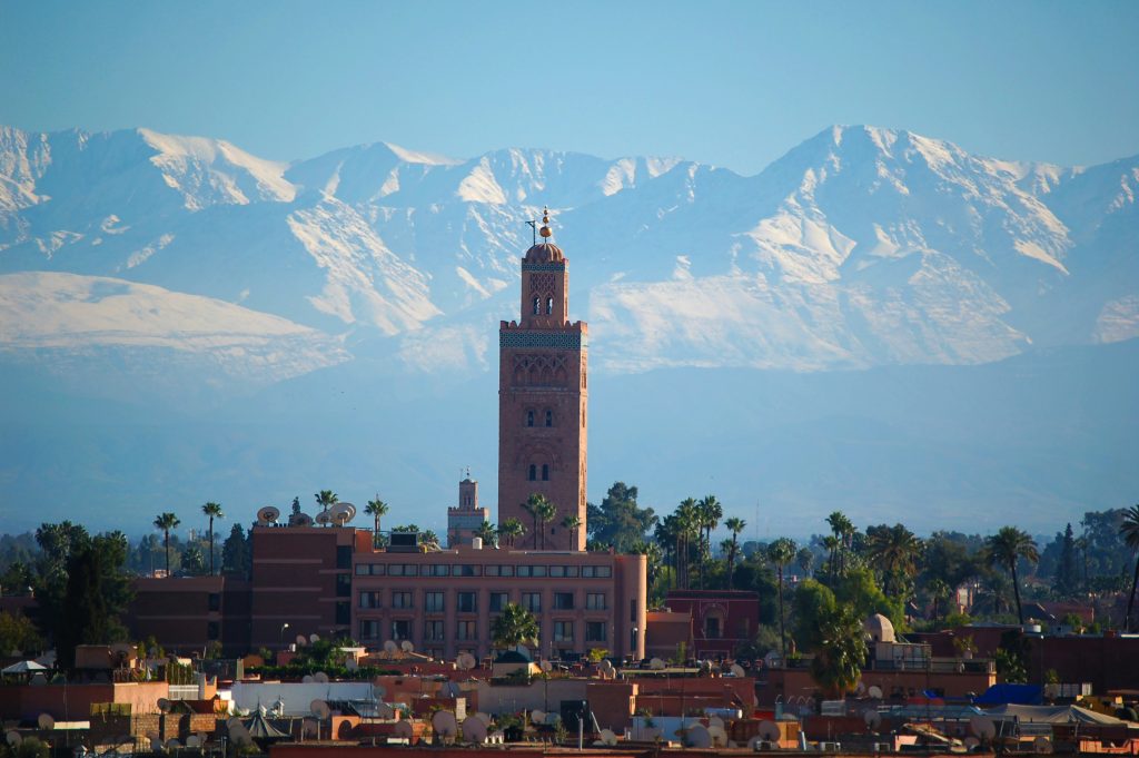 La Koutoubia, emblème de Marrakech, se dresse majestueusement au premier plan avec en toile de fond les sommets enneigés de la chaîne de l’Atlas.