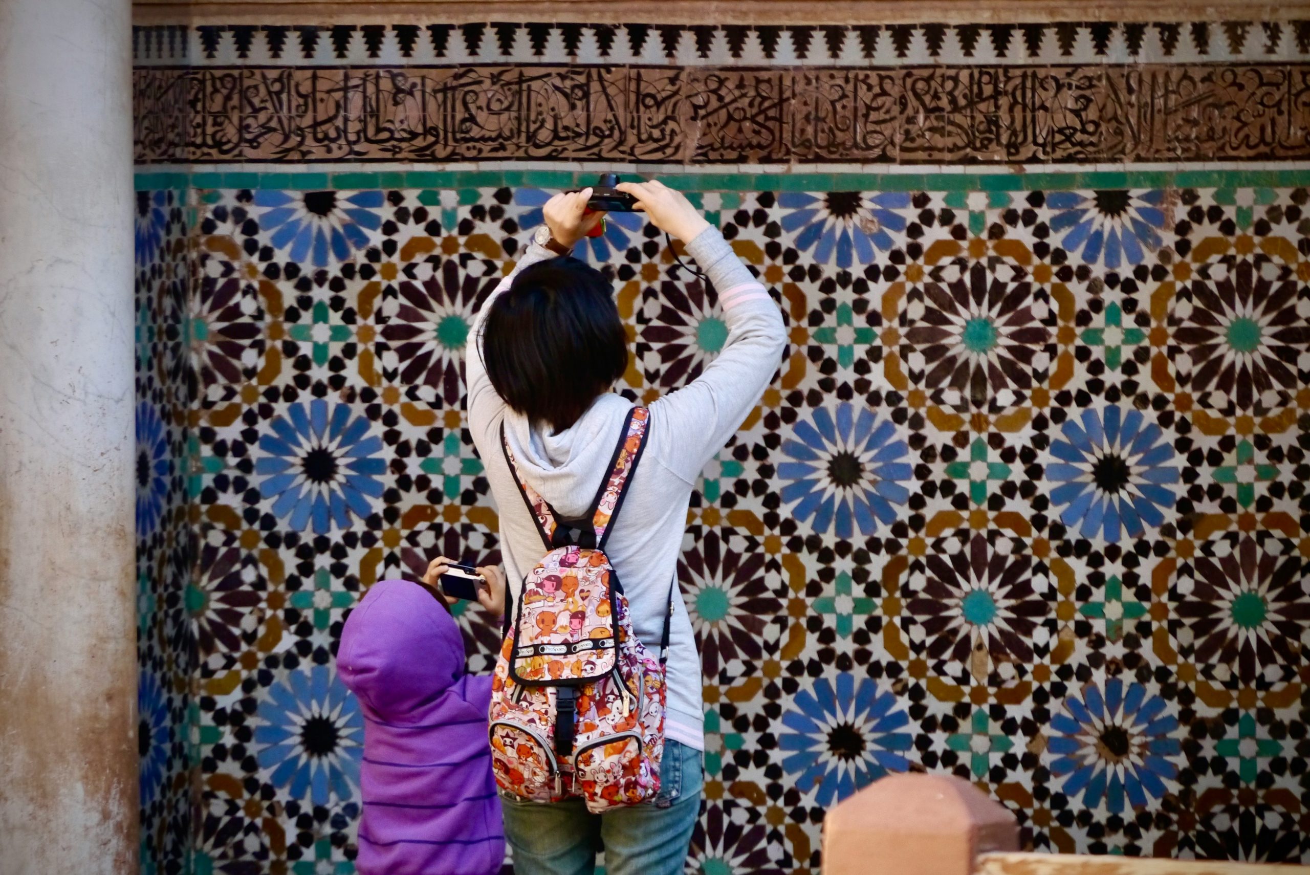Mère et enfant photographiant un mur en zellige marocain à Marrakech, activité familiale typique de la médina.