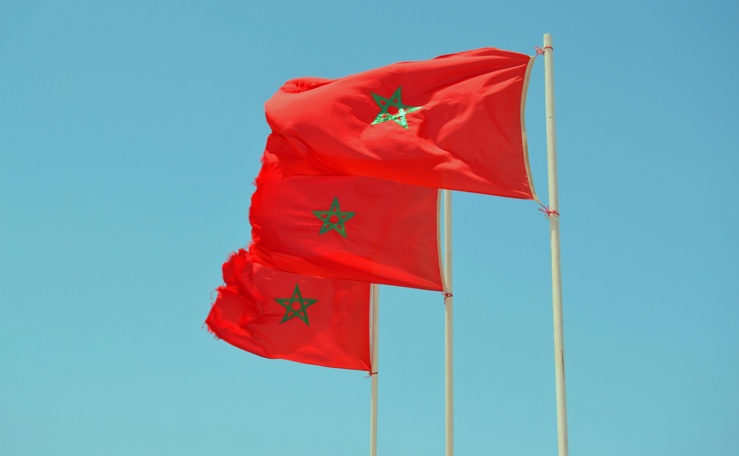 Drapeaux du Maroc flottant dans le ciel bleu, symbole de l’unité nationale et de la souveraineté marocaine.